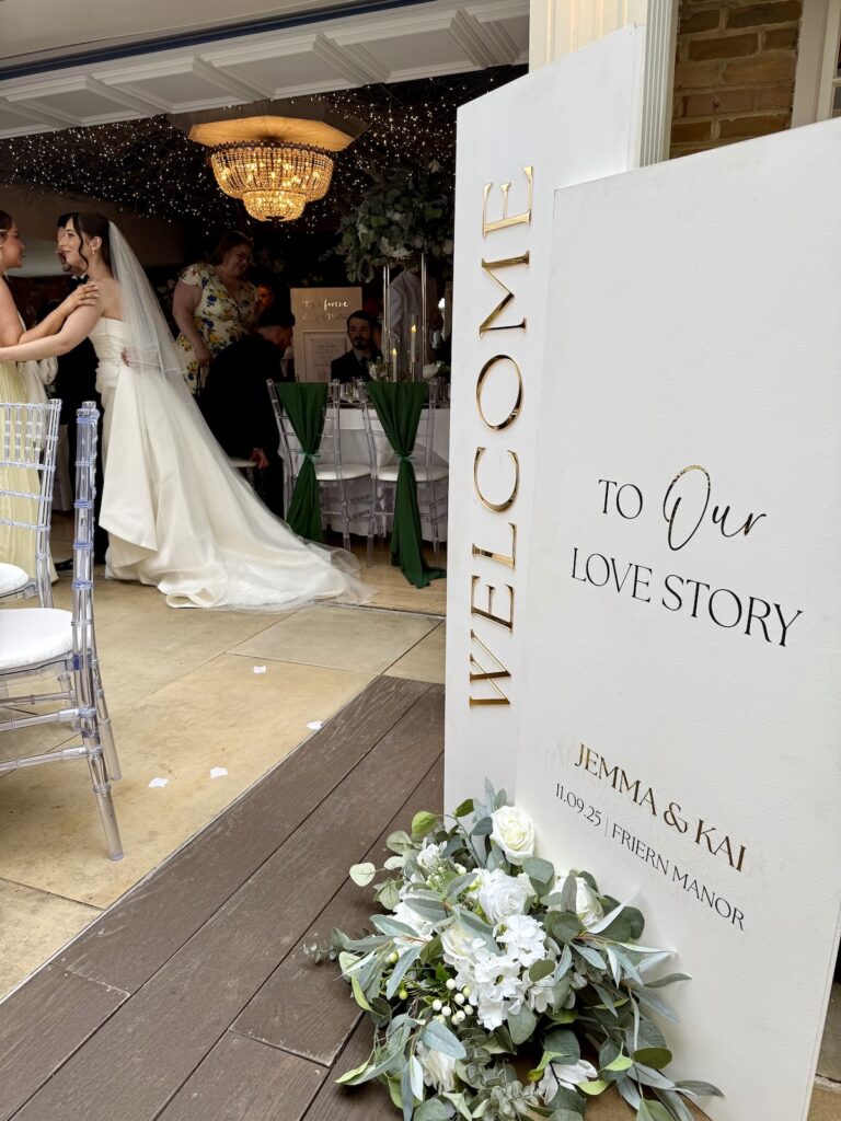 Welcome sign with bride and groom in background at Friern Manor in Essex