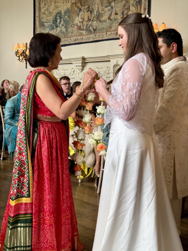Bride being handed Floral necklace by Indian Mother in Law at Elmore Court in Gloucestershire and the Cotswolds