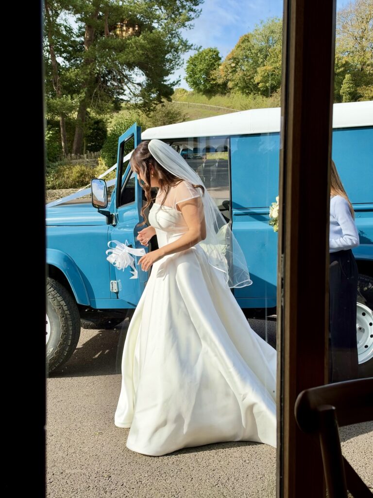 Bride getting out of Landrover at Kingscote barn in The Cotswolds